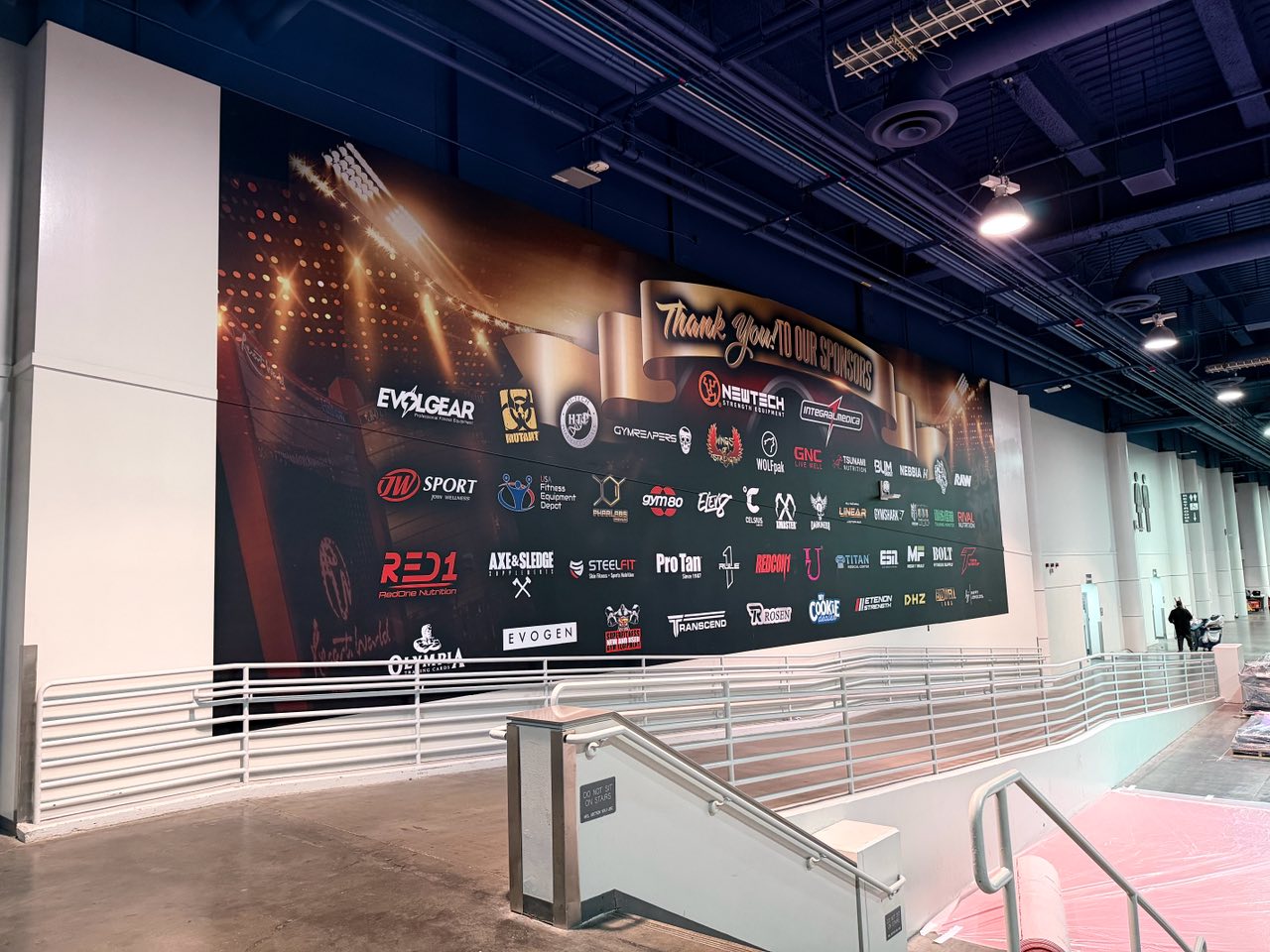 Mr. Olympia sponsor thank-you wall above convention hall stairs